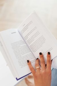From above of anonymous woman with ring on finger resting at home and reading book in daylight